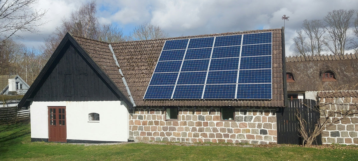Ältere Photovoltaikanlage auf dem Ziegeldach eines Bauernhauses mit Natursteinmauer
