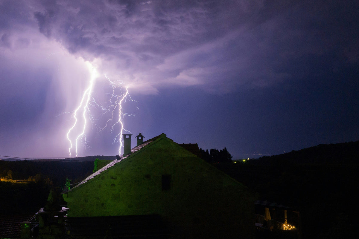 Blitzeinschläge aus einer Gewitterwolke hinter dem Satteldach eines Hauses bei Nacht