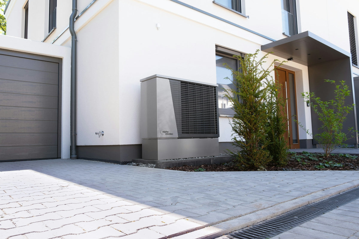 Luft-Wasser-Wärmepumpe vor der weißen Fassade eines modernen Einfamilienhauses neben der Garage