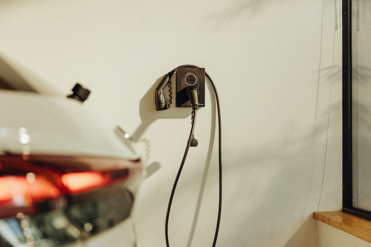 Wandladestation mit Typ-2-Ladekabel an einer hellen Wand, im Vordergrund unscharf das Heck eines Elektroautos