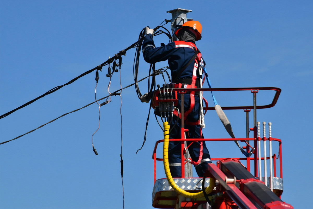 Netzmonteur mit Helm und Sicherungsgurt arbeitet vom Hubsteiger aus an einer Niederspannungs-Freileitung